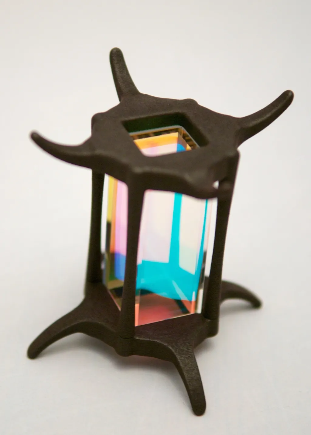 Dark sculpted stand with curved legs holding an iridescent rectangular glass vacuum cell