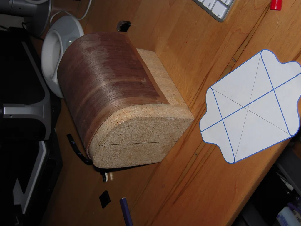 Top-down view of the foam forming block wrapped in walnut veneer, next to a paper shell template marked with layout lines