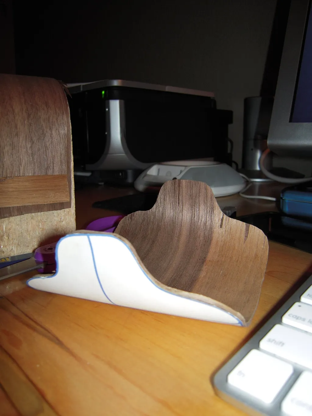 A formed walnut-veneer shell piece with its paper template pressed against it, beside the veneered forming block