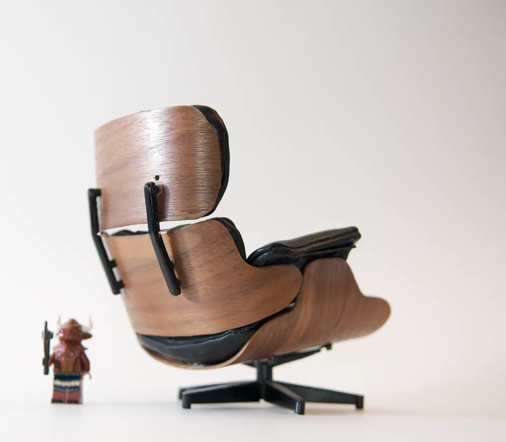 Rear view of the scale Eames Lounge Chair model, showing walnut-veneer shells, black spines and a five-star base, with a Lego minifigure beside it for scale