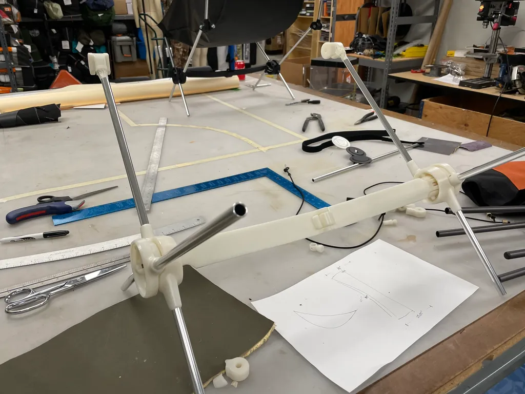Folding chair frame prototype on a workbench, with aluminum poles joined by white 3-D printed hubs