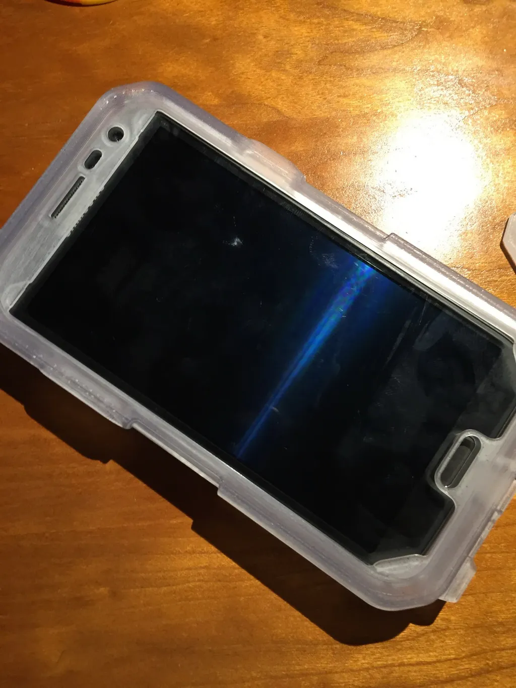 Clear prototype case fitted on a smartphone, lying on a wooden table
